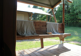 Blick aus einem Safarizelt mit Holzterrasse und Bank bei Tolne Camping, Dänemark, im Grünen.