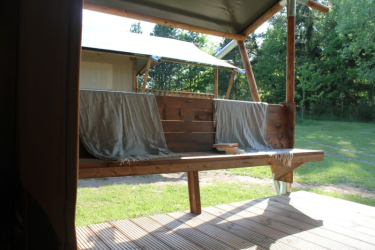 Blick aus einem Safarizelt mit Holzterrasse und Bank bei Tolne Camping, Dänemark, im Grünen.