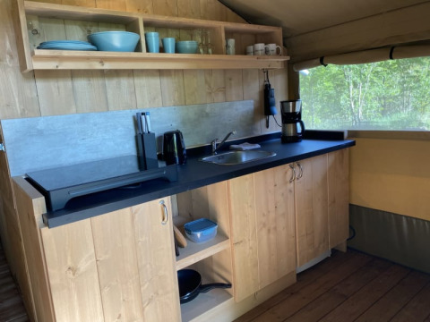 Zona de cocina dentro de un safari tent en Tolne Camping, Dinamarca, con vajilla y cafetera visible.