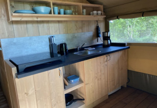 Zona de cocina dentro de un safari tent en Tolne Camping, Dinamarca, con vajilla y cafetera visible.