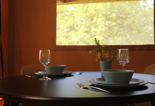 Mesa preparada para dos personas en una tienda safari con ventana y vista natural en Tolne Camping, Dinamarca.