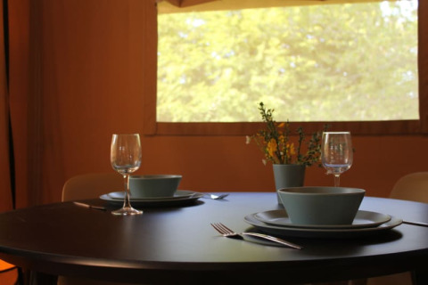 Table set for two inside a safari tent with a window view of nature at Tolne Camping, Denmark.