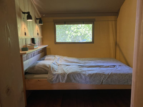 Acogedora zona de dormitorio en tienda safari con cama, lámparas y ventana en Tolne Camping, Dinamarca.