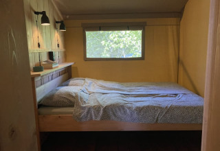 Acogedora zona de dormitorio en tienda safari con cama, lámparas y ventana en Tolne Camping, Dinamarca.