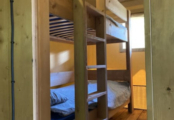 Køjeseng i træ i et safari telt med badeværelse på Tolne Camping i Danmark, set fra døråbningen.