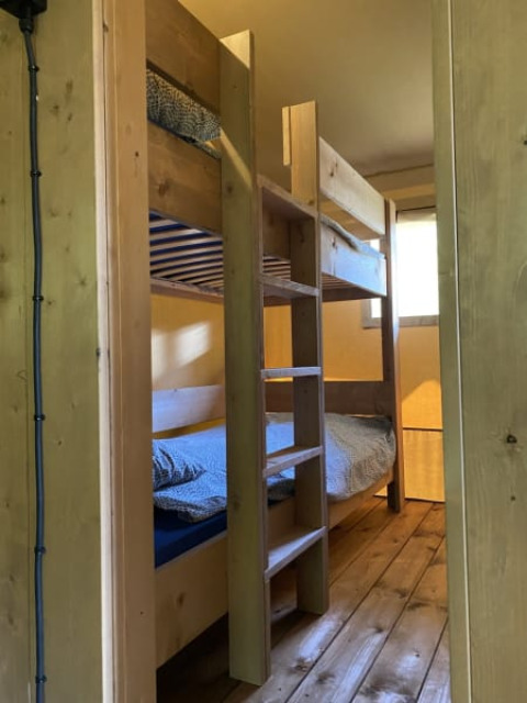 Letto a castello in legno in tenda safari con bagno al Tolne Camping in Danimarca, visto dalla porta.