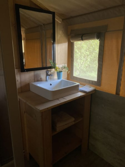 Wastafel met spiegel en handdoeken in een safaritent met sanitair op Tolne Camping in Denemarken.