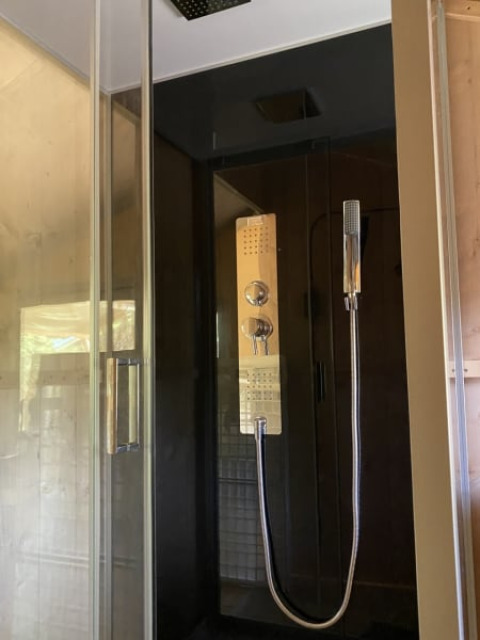 Ducha moderna con puerta de cristal y pared oscura, en tienda safari con baño privado en Tolne Camping, Dinamarca.