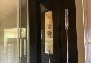 Ducha moderna con puerta de cristal y pared oscura, en tienda safari con baño privado en Tolne Camping, Dinamarca.