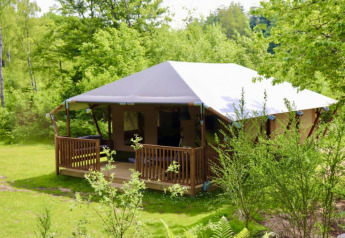 Tienda glamping tipo safari con baño privado en Tolne Camping, Dinamarca, rodeada de naturaleza verde.
