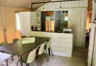 Interior de una tienda glamping con mesa de comedor, sillas y cocina en Tolne Camping, Dinamarca.