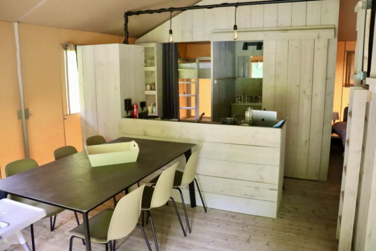 Interior de una tienda glamping con mesa de comedor, sillas y cocina en Tolne Camping, Dinamarca.