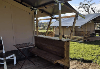 Tente safari avec terrasse en bois et meubles simples au Minicamping MiO en Allemagne, vue sur d’autres tentes.