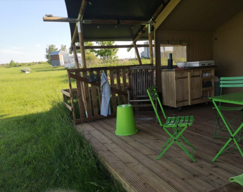 Außenterrasse eines Safarizeltes bei Minicamping MiO in Deutschland mit grünen Stühlen und Landschaft.