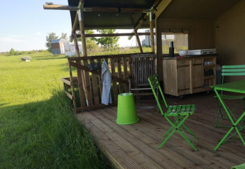 Udendørs terrasse ved en safaritelt på Minicamping MiO i Tyskland med grønne stole og landlig udsigt.