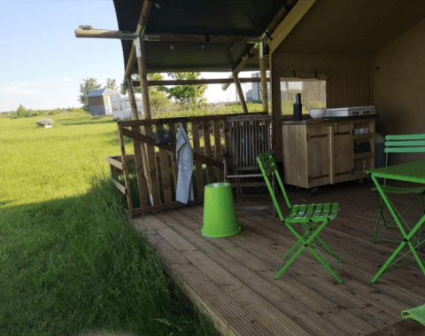 Veranda esterna di una tenda safari a Minicamping MiO in Germania con sedie verdi e vista sulla campagna.