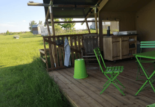 Terrasse extérieure d'une tente safari au Minicamping MiO en Allemagne avec chaises vertes et vue champêtre.