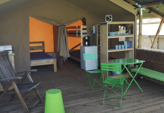 Safari tent at Minicamping MiO in Germany featuring green chairs, bunk beds, and an open sitting area.