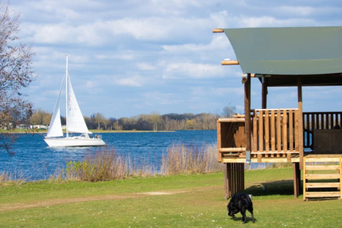 Safarizelt mit Sanitäranlagen im Recreatiepark Riverside, Niederlande, mit Blick auf See und Segelboot.
