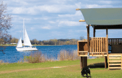 Safari tent with sanitary facilities at Recreatiepark Riverside in the Netherlands, lakeside view with sailboat.