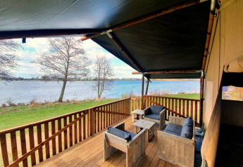 Terrasse med træmøbler og udsigt over søen ved en safaritelt med bad på Recreatiepark Riverside.