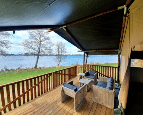 Terrasse med træmøbler og udsigt over søen ved en safaritelt med bad på Recreatiepark Riverside.