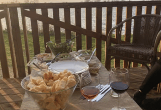 Udendørs spisebord med vin, brød og snacks på terrasse i Safari-telt ved søen i Riverside, Holland.