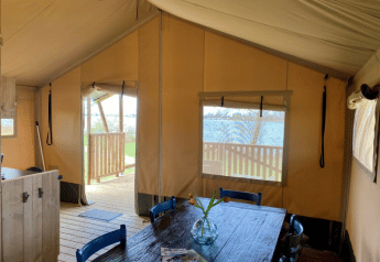 Intérieur de la tente Safari tent + sanitary au Recreatiepark Riverside, Pays-Bas, avec table à manger.