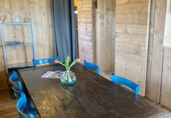 Zona pranzo in una tenda safari con pareti di legno, tavolo scuro, sedie blu e vaso di fiori in Olanda.