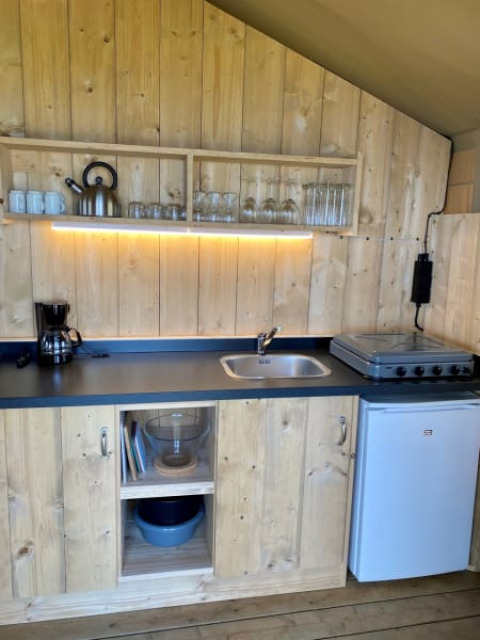 Cocina con paneles de madera en Safari tent + sanitary de Recreatiepark Riverside, Países Bajos, con estufa y nevera.