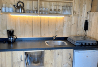 Wood-paneled kitchenette in Safari tent + sanitary at Recreatiepark Riverside, Netherlands, with stove and fridge.