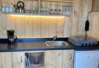 Wood-paneled kitchenette in Safari tent + sanitary at Recreatiepark Riverside, Netherlands, with stove and fridge.