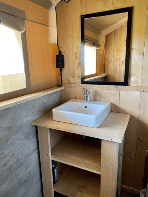 Lavabo con espejo y paredes de madera en una tienda safari en Recreatiepark Riverside, Países Bajos.