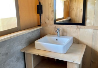 Lavabo con espejo y paredes de madera en una tienda safari en Recreatiepark Riverside, Países Bajos.