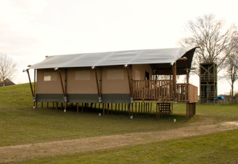 Safari-telt med sanitære faciliteter på pæle ved Recreatiepark Riverside i Holland, omgivet af græs.