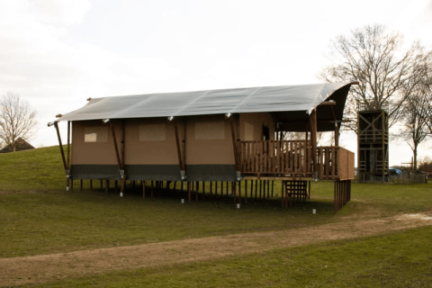 Safari-Zelt mit Sanitäranlagen auf Stelzen im Recreatiepark Riverside in den Niederlanden, auf Grasland.