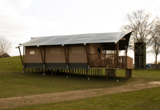 Safaritent met eigen sanitair op palen bij Recreatiepark Riverside in Nederland, omringd door grasveld.