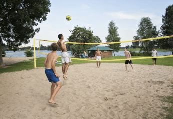 Unge mænd spiller beachvolleyball på sandet ved en sø i nærheden af Safari telt med sanitær i Riverside, Holland.