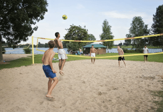 Giovani giocano a beach volley su sabbia vicino a tenda Safari con servizi igienici a Riverside, Paesi Bassi.