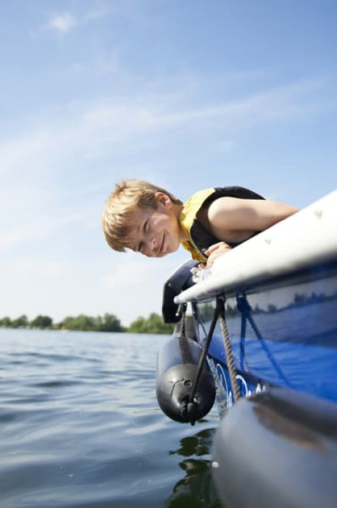 Junge mit Schwimmweste lehnt sich über ein Boot am Safari-Zelt mit Bad im Recreatiepark Riverside, Niederlande.