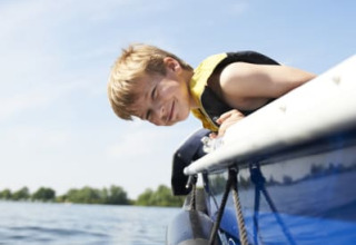 Junge mit Schwimmweste lehnt sich über ein Boot am Safari-Zelt mit Bad im Recreatiepark Riverside, Niederlande.
