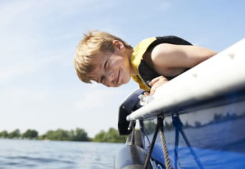 Ragazzo con giubbotto di salvataggio si sporge da una barca presso la Safari tent + sanitary a Recreatiepark Riverside, Paesi Bassi.