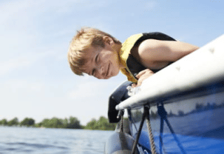 Boy in life jacket leaning over a boat by the Safari tent with sanitary at Recreatiepark Riverside, Netherlands.
