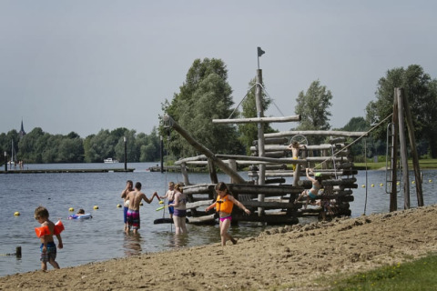 Kinder spielen im Wasser am Sandstrand mit Piratenschiff-Spielplatz bei Recreatiepark Riverside, Niederlande.