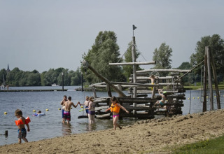 Enfants en gilets de sauvetage jouent sur une plage avec un bateau en bois au Recreatiepark Riverside.