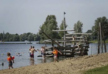 Enfants en gilets de sauvetage jouent sur une plage avec un bateau en bois au Recreatiepark Riverside.