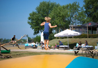 Bambini giocano su un cuscino elastico vicino a una tenda safari con servizi igienici al Recreatiepark Riverside, Paesi Bassi.