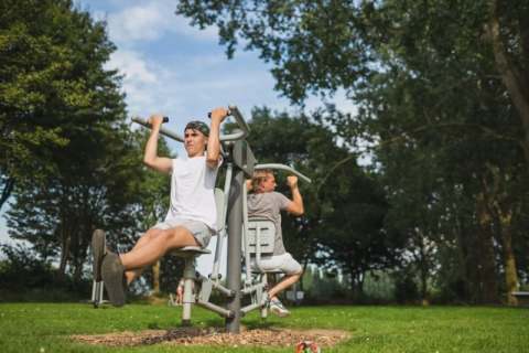Zwei Personen trainieren an Outdoor-Fitnessgeräten beim Safari-Zelt mit Sanitäranlagen im Recreatiepark Riverside, Niederlande.