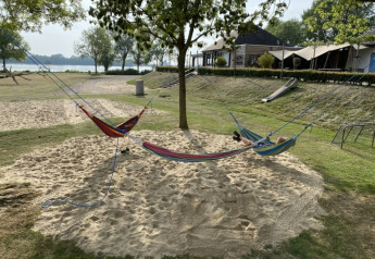 Drei Hängematten hängen im Sand unter Bäumen beim Safarizelt mit Sanitär am Recreatiepark Riverside.