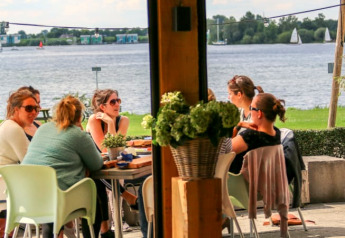 Gruppe mennesker sidder ved bord under en safari-telt ved vandet i Recreatiepark Riverside, Holland.